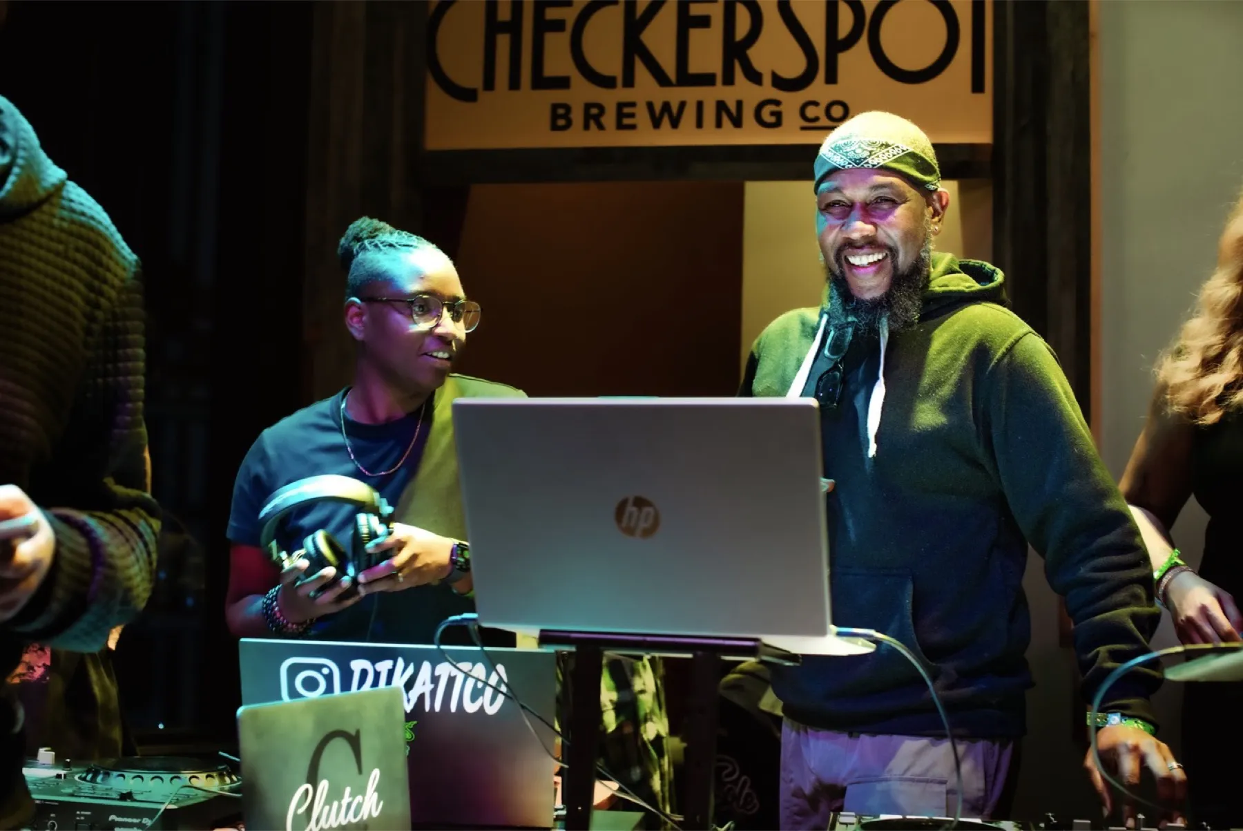 DJs spinning in front of the Checkerspot sign